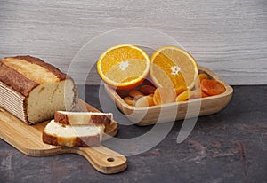 Orange cake on a kitchen board with a sliced Ã¢â¬â¹Ã¢â¬â¹orange and apricot in a wooden bowl, copy space